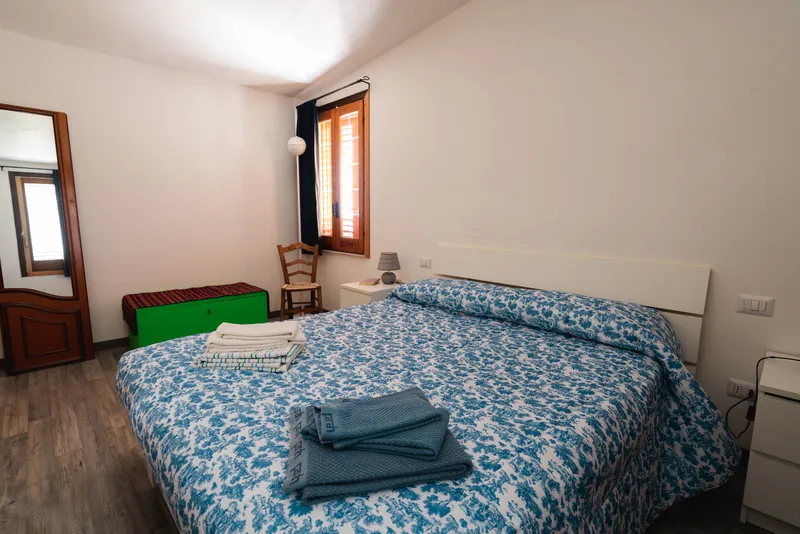 Camera con letto matrimoniale, copriletto a fiori blu e porta aperta sulla luce
