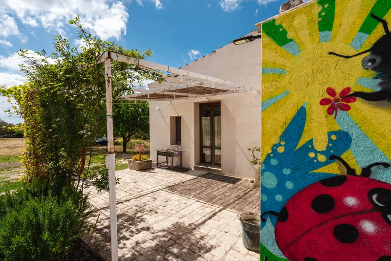 Ingresso della casa con pergolato, piante e un murale giallo e turchese