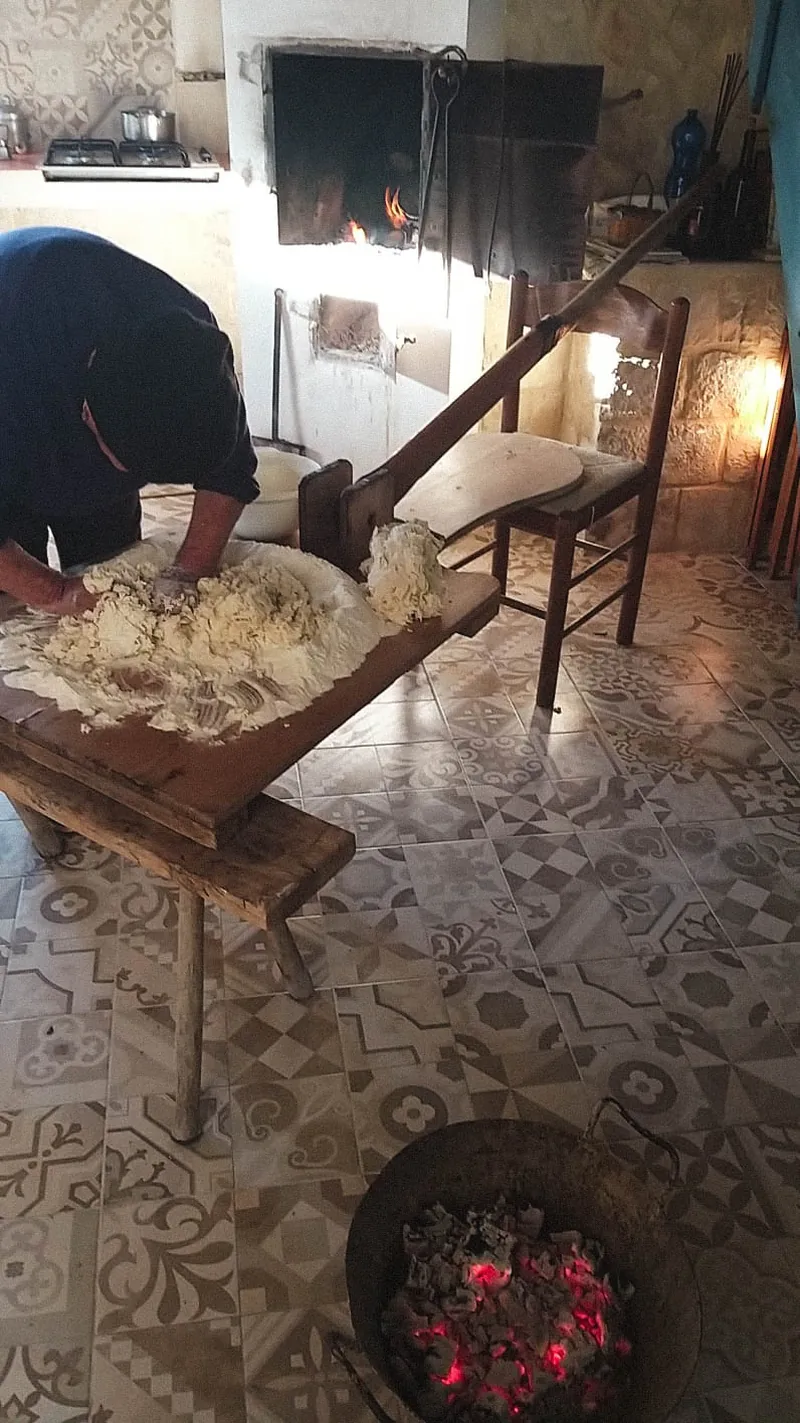 Una persona lavora l’impasto sul tavolo davanti al forno a legna