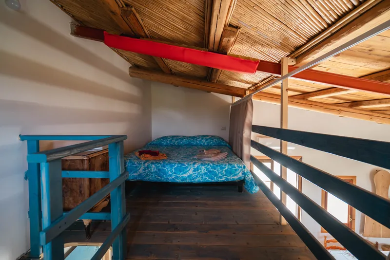 Letto sul soppalco con travi a vista e ringhiera turchese